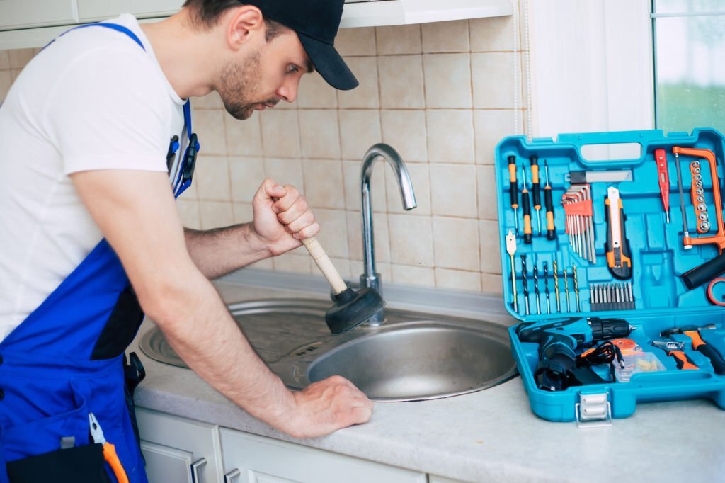 Handyman in uniform is cleaning a clogged kitchen sink with the help of plunger