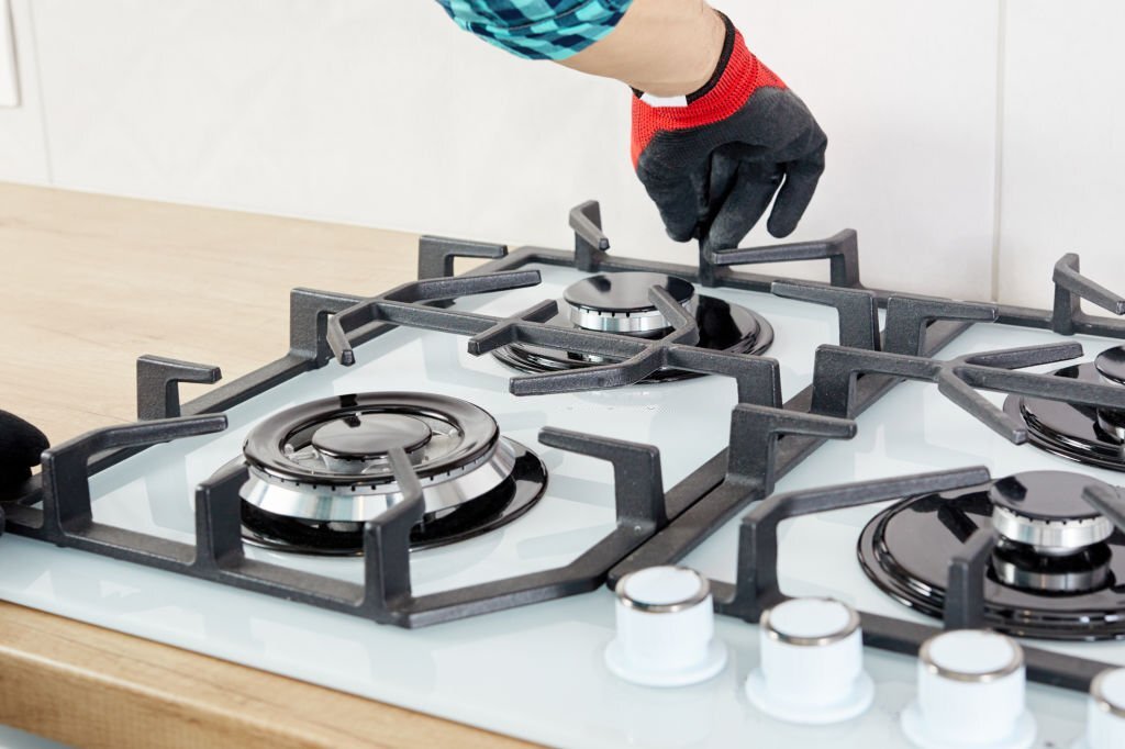 Repairs and fixing of gas control panel. Man hand in protective gloves repairs hotplate of a hob.